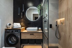 A modern bathroom with a washing machine, a sink with a mirror, and a shower area.