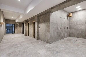 Ein moderner Flur mit grauen Fliesenböden und -wänden, mit einer Holztür und einem kleinen Holz-Eimer an der Wand.