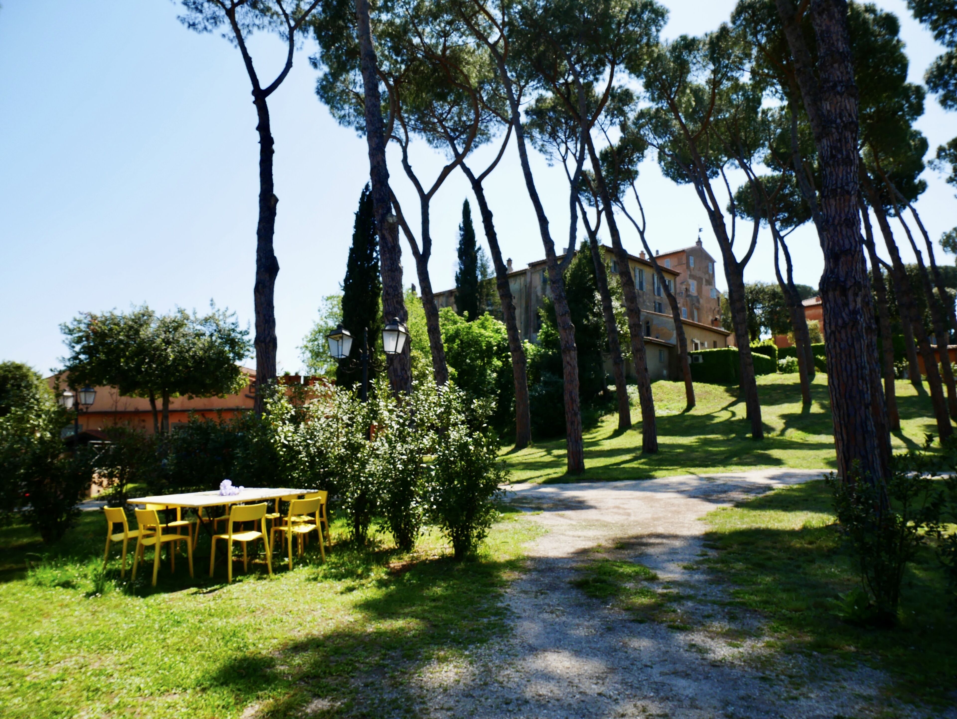 A pathway leading to a building surrounded by trees and a grassy area with a table and chairs.