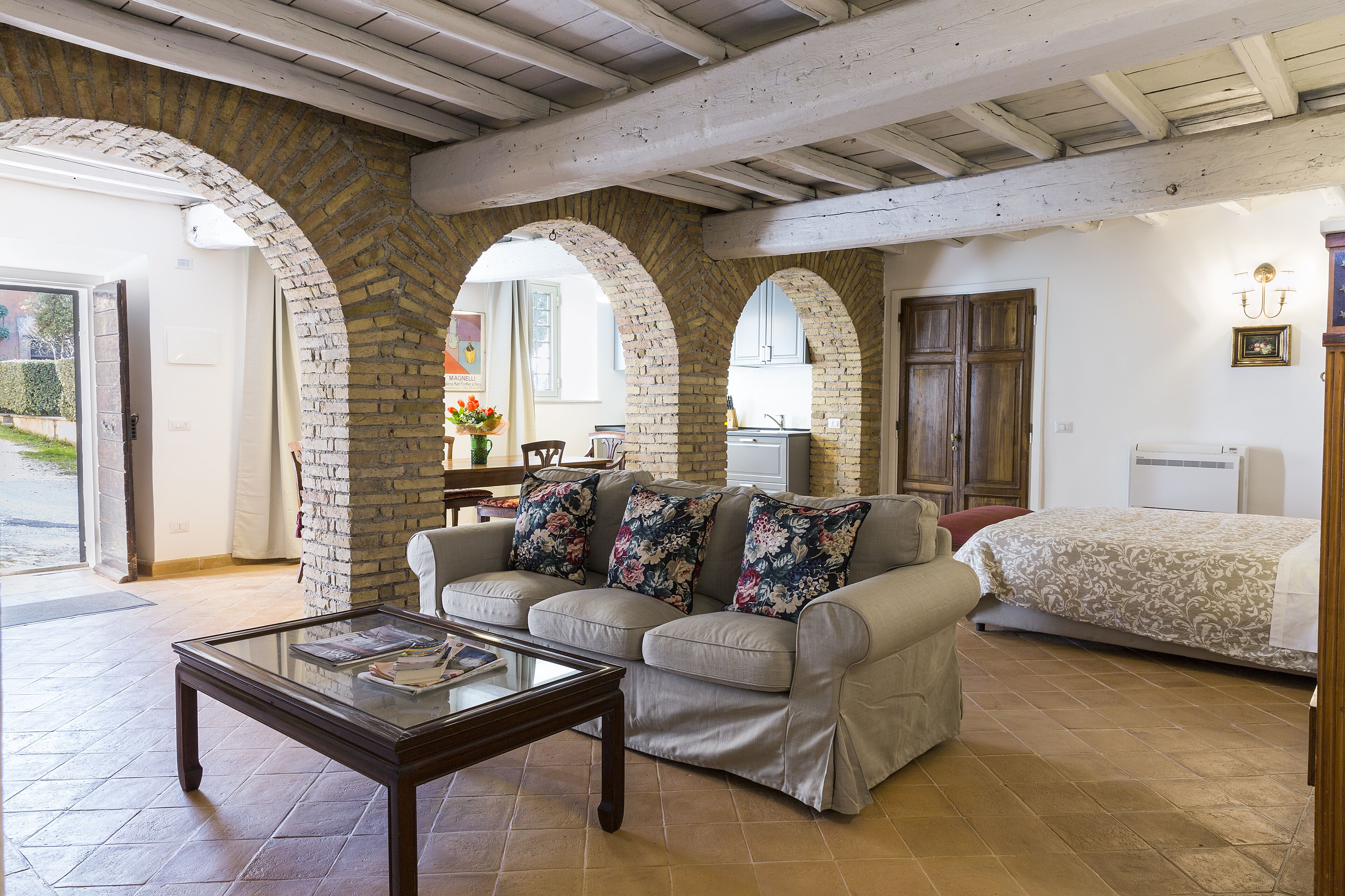 Una sala de estar con sofá, mesa de centro y cama. Se observan arcos de ladrillo y techo de madera.