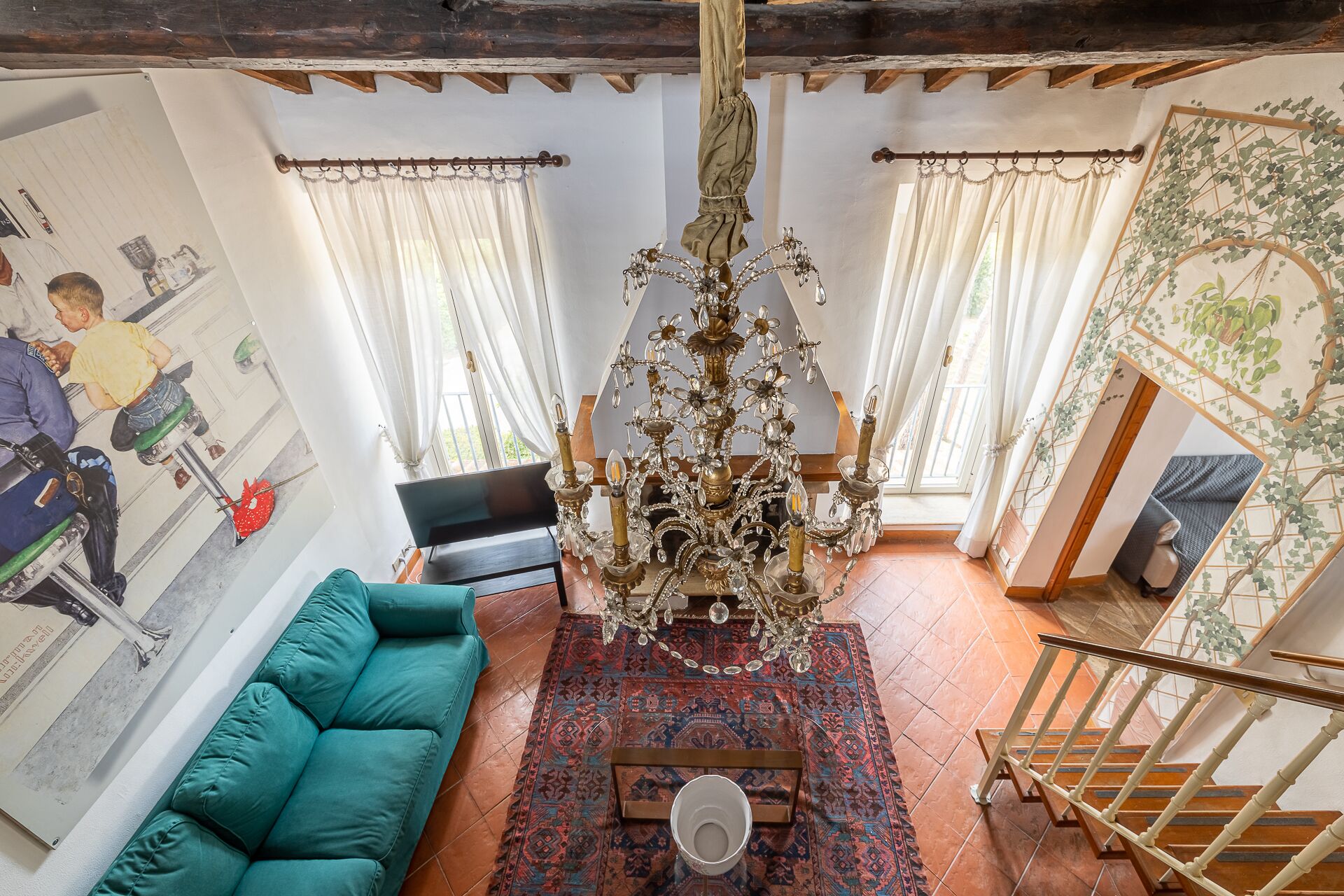 Uma sala de estar com um candelabro, um sofá verde, um tapete estampado e uma escada.