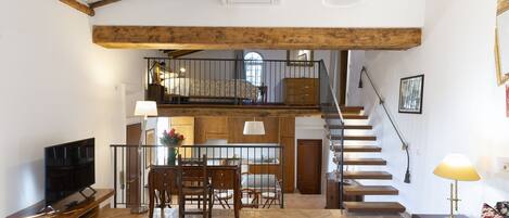 Un amplio salón con una escalera de madera, una mesa de comedor con sillas, un televisor y un sofá.