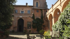 A courtyard with a building featuring a tower, arched windows, and a gate. - Castello del Duca (Rome)