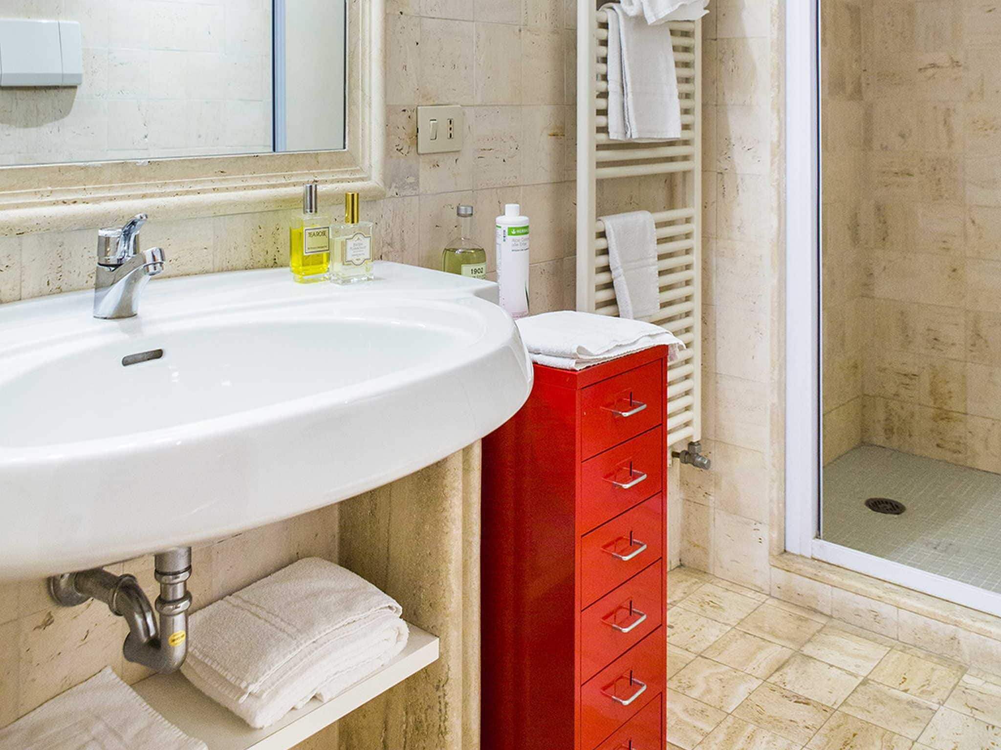 A bathroom with a white sink, red storage cabinet, and a mirror.