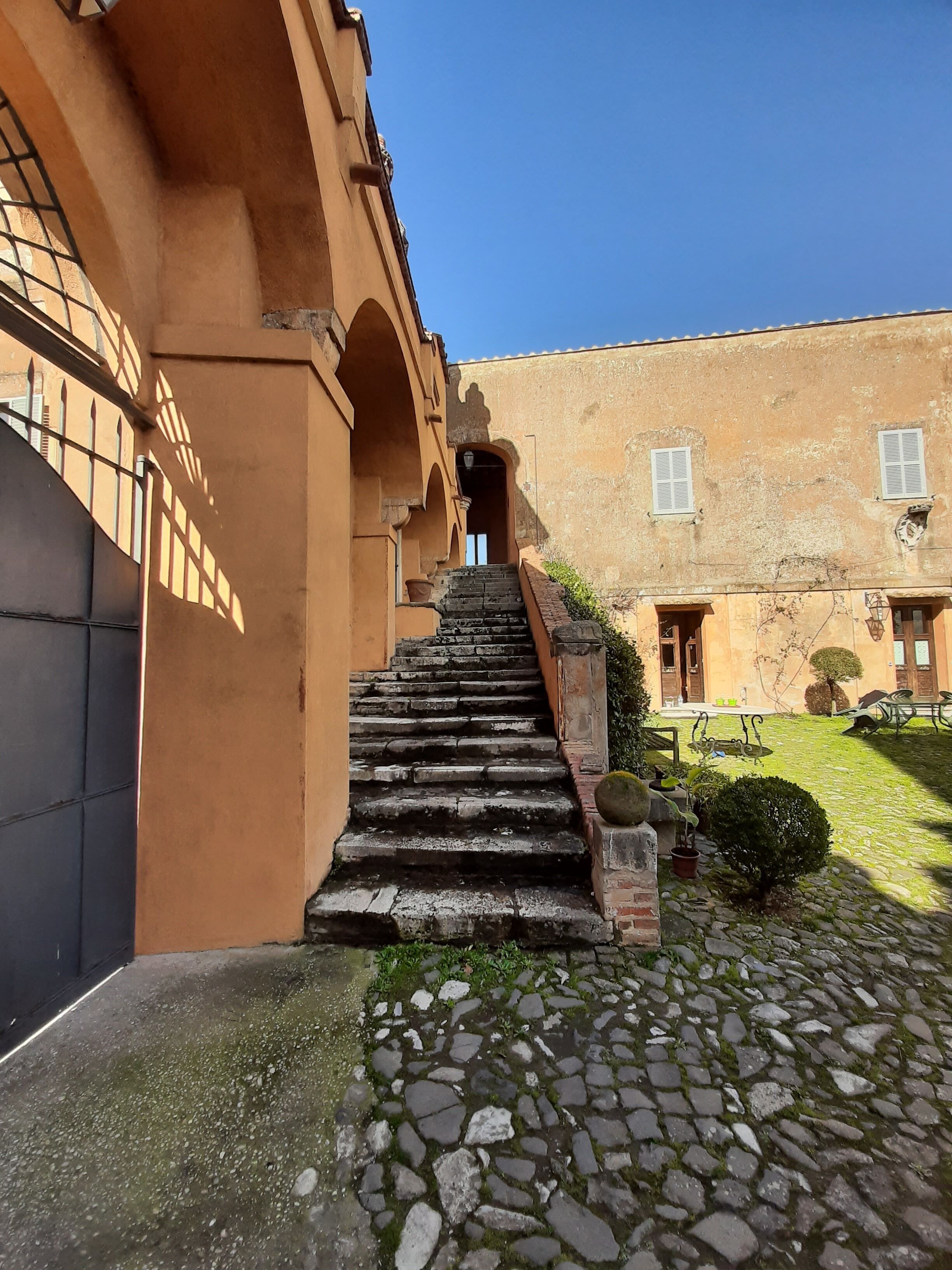 Una escalera de piedra conduce a un edificio con arcos y un patio con mesa y sillas.