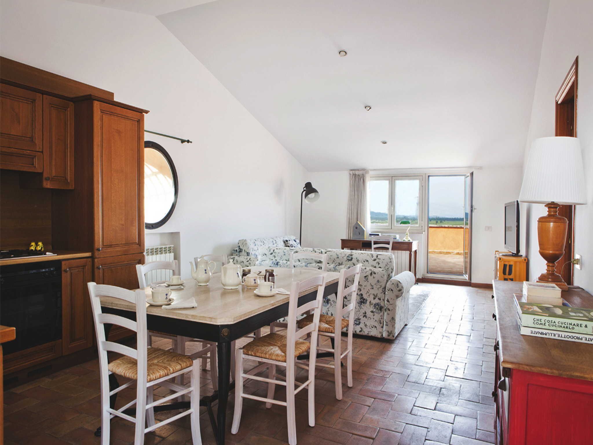 Une cuisine chaleureuse avec des meubles en bois, une table à manger entourée de chaises et une vue sur la mer grâce à de grandes fenêtres.