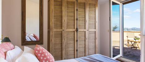 A bedroom with a bed, a large wardrobe, a mirror, and a sliding glass door to a balcony.