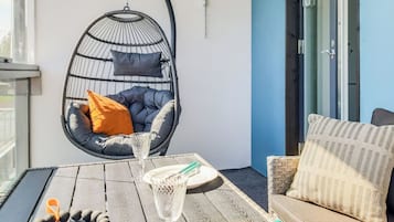 A balcony with a hanging chair, a table with a glass, a plate, and a bracelet.