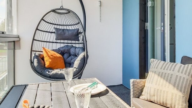 A cozy outdoor seating area with a hanging chair, a wooden table set with plates, glasses, and cutlery, and a sofa with cushions.