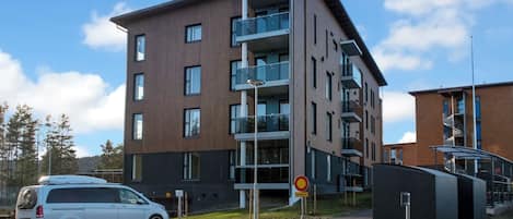 A modern multi-story building with balconies and a parking area.