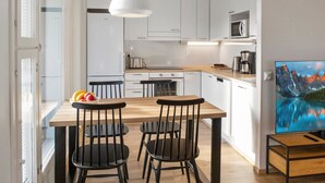 A modern kitchen with white cabinets, a wooden dining table, and black chairs. There is a painting of a mountain landscape on the wall.