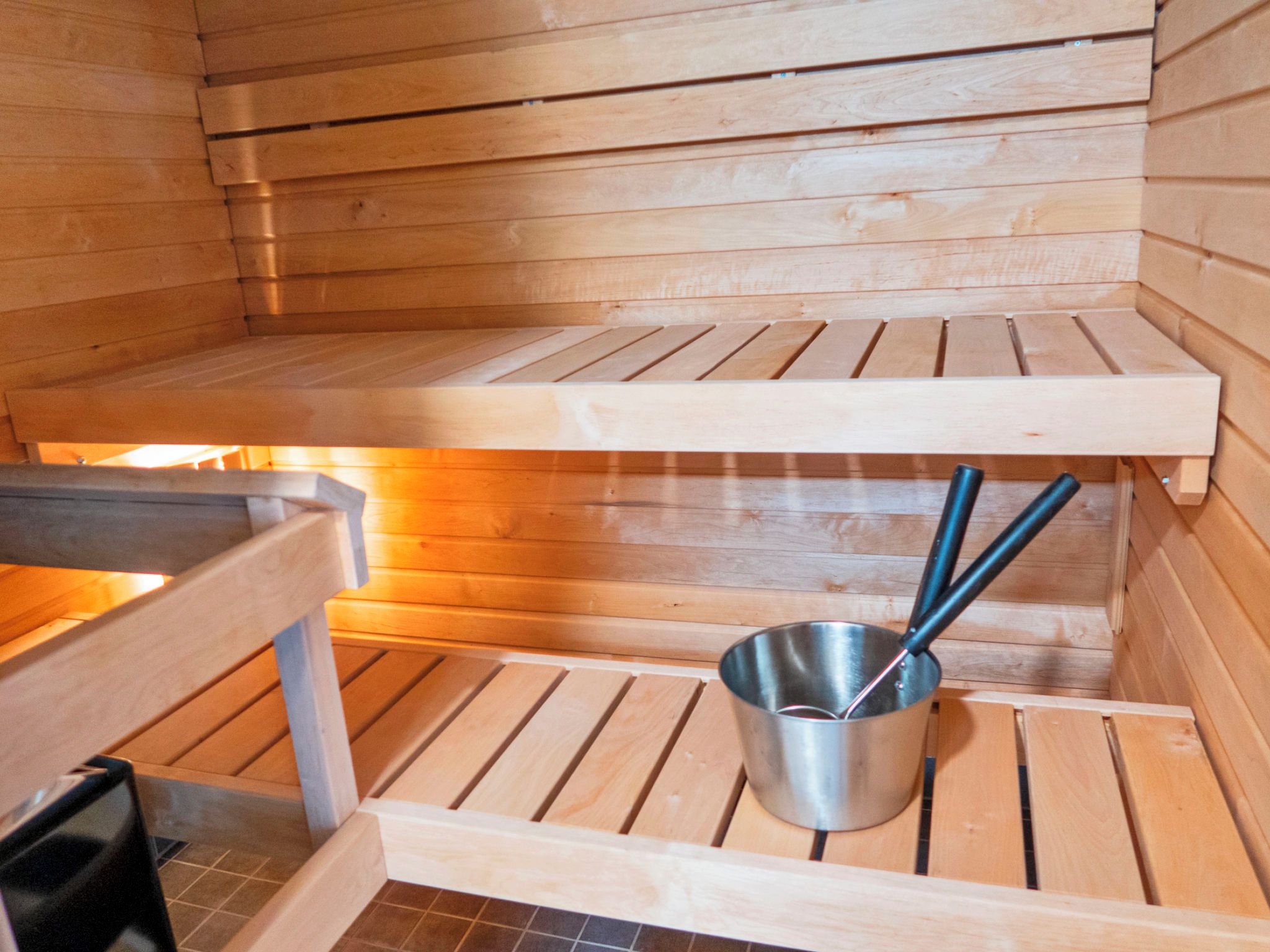 A sauna with wooden benches and a metal bucket with a ladle.