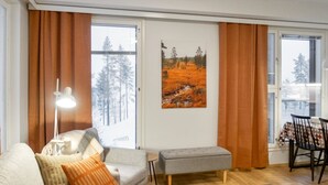 A living room with a sofa, a table, a lamp, a painting, and a view of trees through the window.