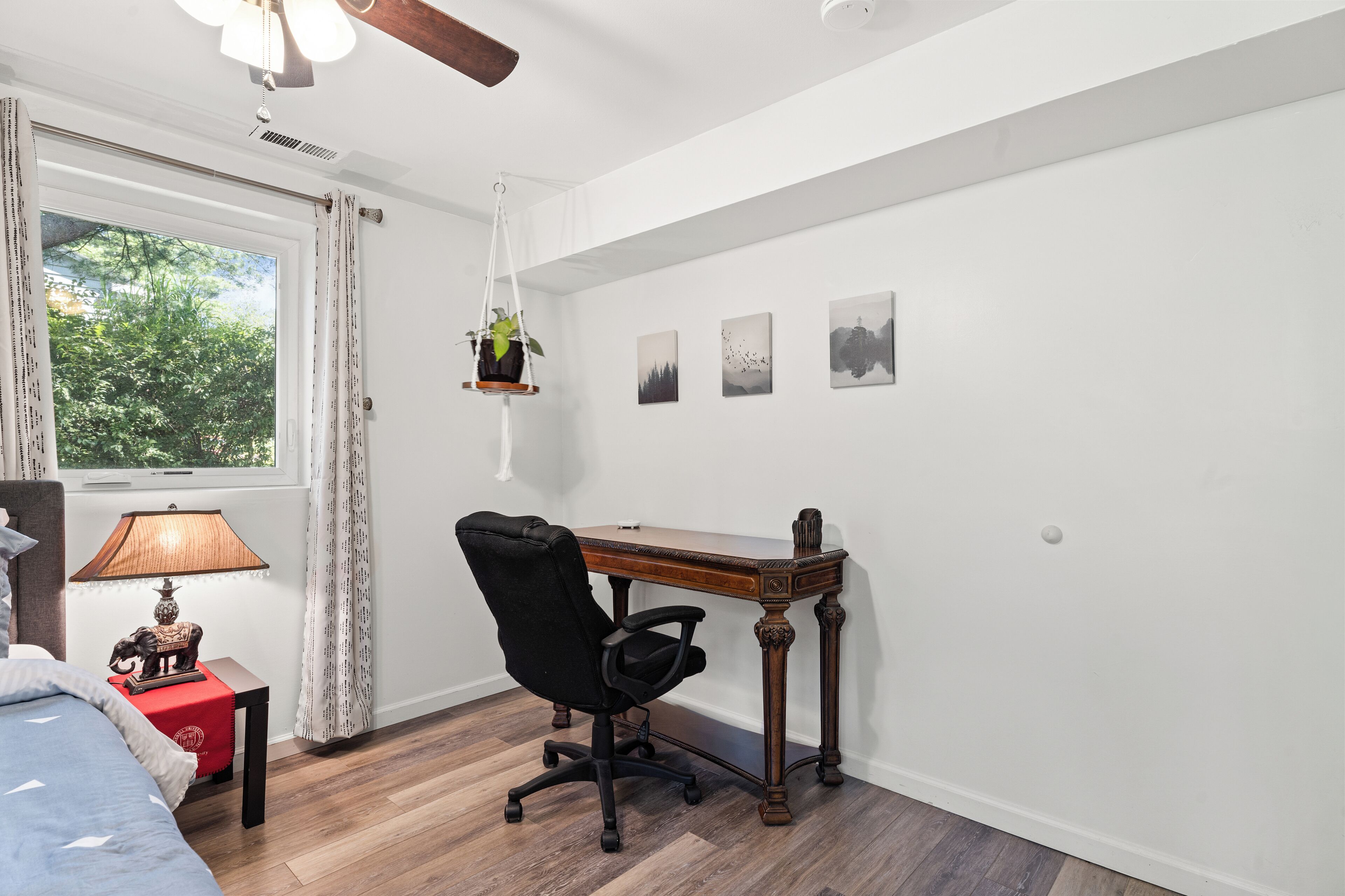 Een slaapkamer met een bed, bureau, stoel, lamp en een raam met gordijnen.