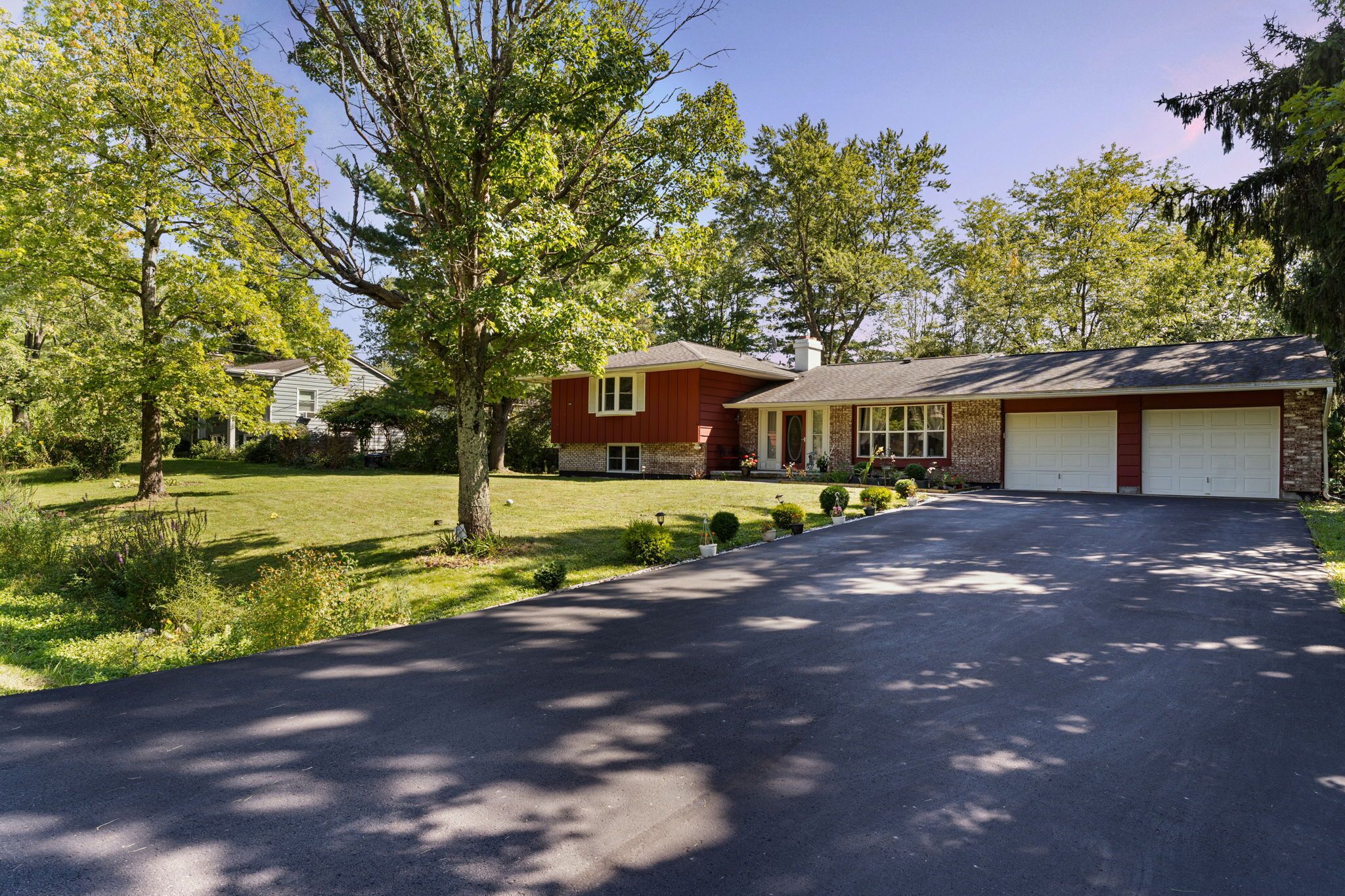 A residential driveway leading to a house with a garage, surrounded by trees and a well-maintained lawn.