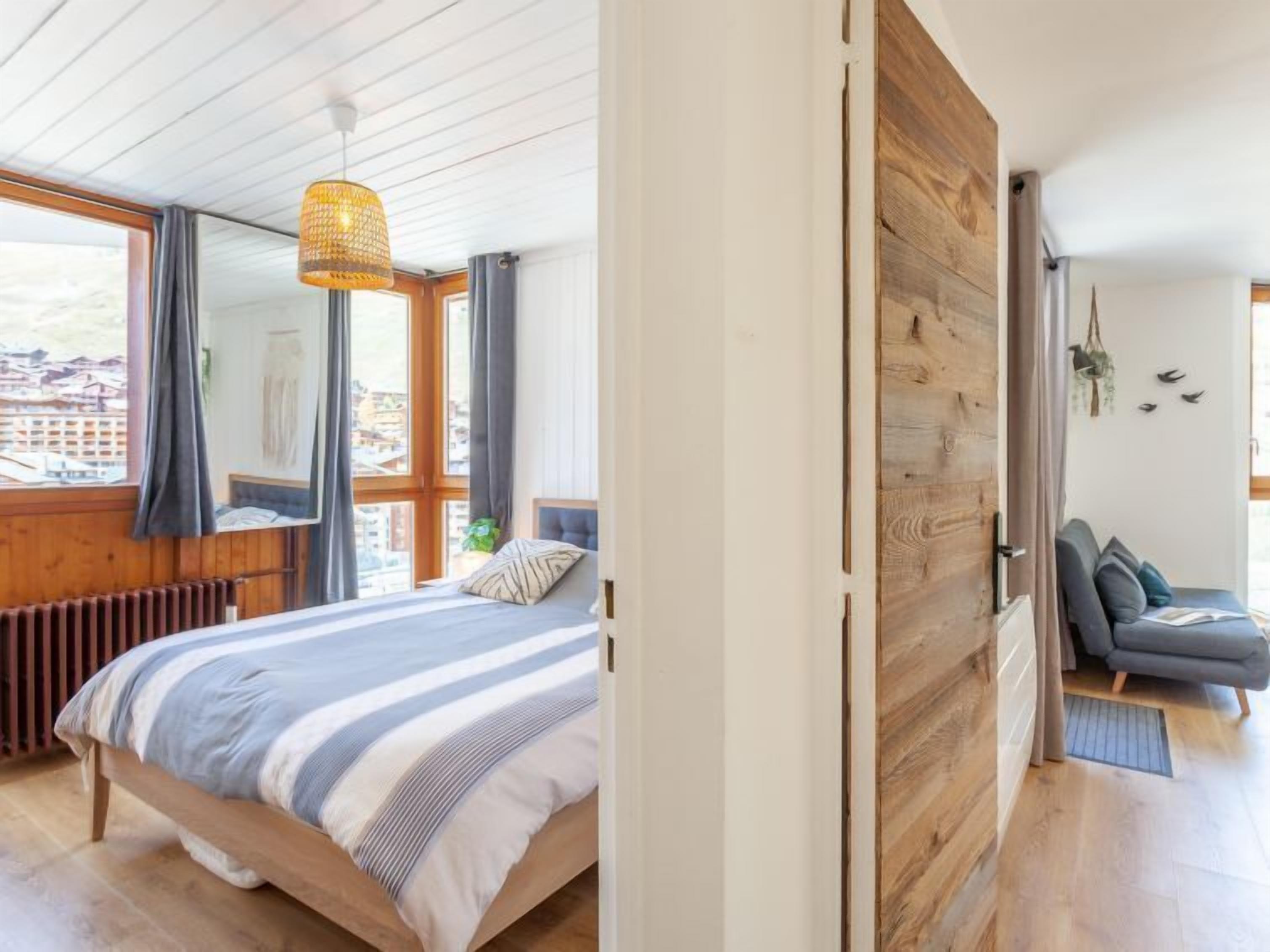 Une chambre à coucher avec un grand lit, une fenêtre avec des rideaux, un luminaire suspendu et une vue sur la ville.