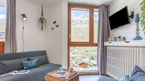 A modern living room with a grey sofa, a wooden chest, and a view of a mountainous landscape through large windows. - Savoy (Lavachet) by Interhome (Tignes)