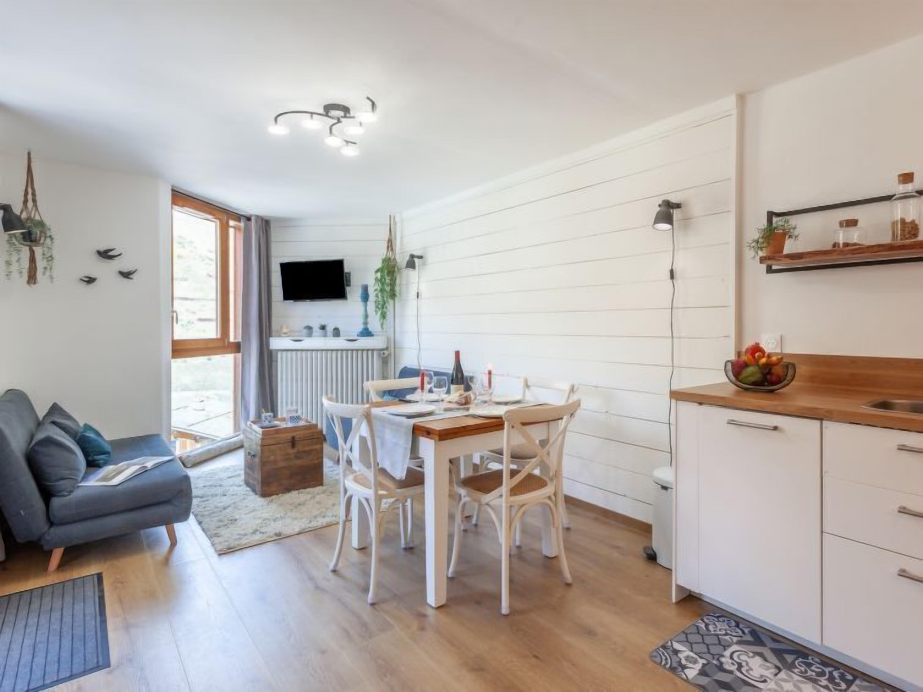 Une cuisine moderne avec des meubles blancs, une table à manger entourée de chaises blanches et un four encastré.