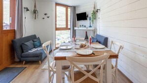 A cozy dining area with a wooden table set for four, white chairs, and a grey sofa in the background. - Savoy (Lavachet) by Interhome (Tignes)
