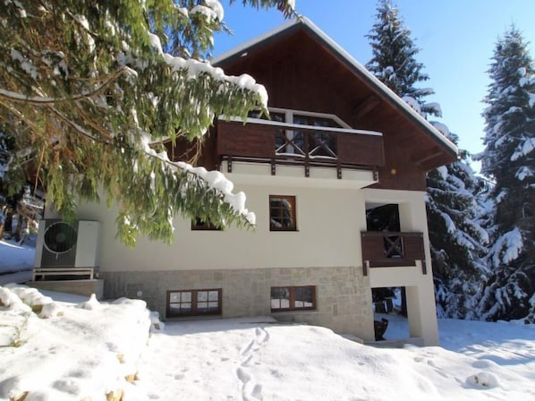 Un chalet à deux étages, avec une façade en bois, des fondations en pierre et un balcon.