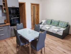 A compact living space with a kitchenette, a dining table with chairs, and a sofa with patterned cushions.