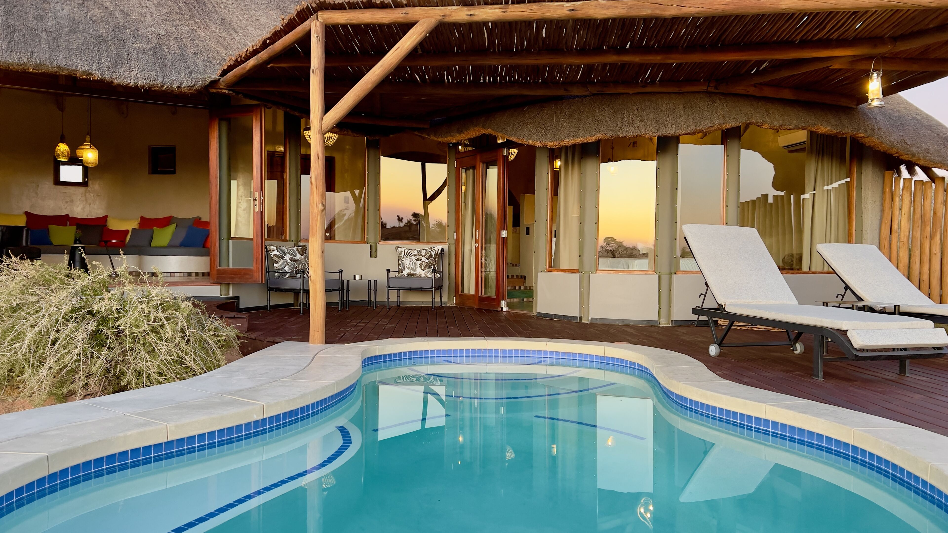 Un área de piscina con sillones de descanso, una estructura de techo de paja y vista al atardecer.