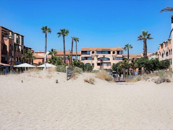 A beachfront hotel with multiple floors, palm trees, and a sandy beach.