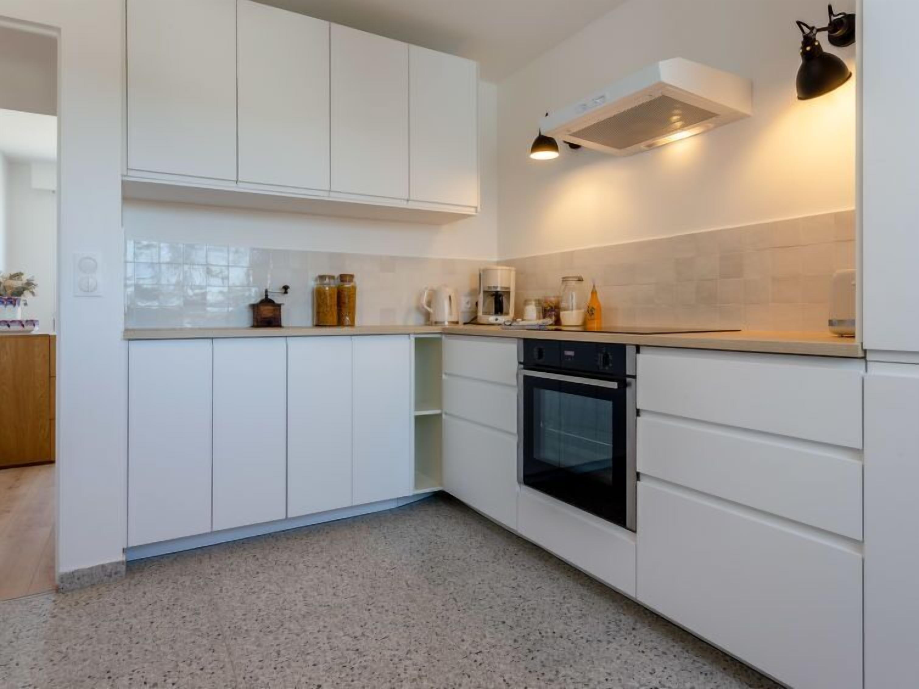 A modern kitchen with white cabinets, a built-in oven, and a countertop with various appliances and jars.