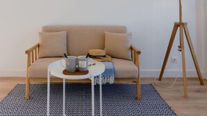 Ein gemütliches Wohnzimmer mit einem beigen Sofa, einem kleinen runden Tisch mit zwei Tassen, einer Lampe und drei gerahmten Bildern an der Wand.
