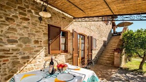 Un edificio de piedra con una mesa dispuesta para comer, que incluye una botella de vino, fruta y cubiertos.