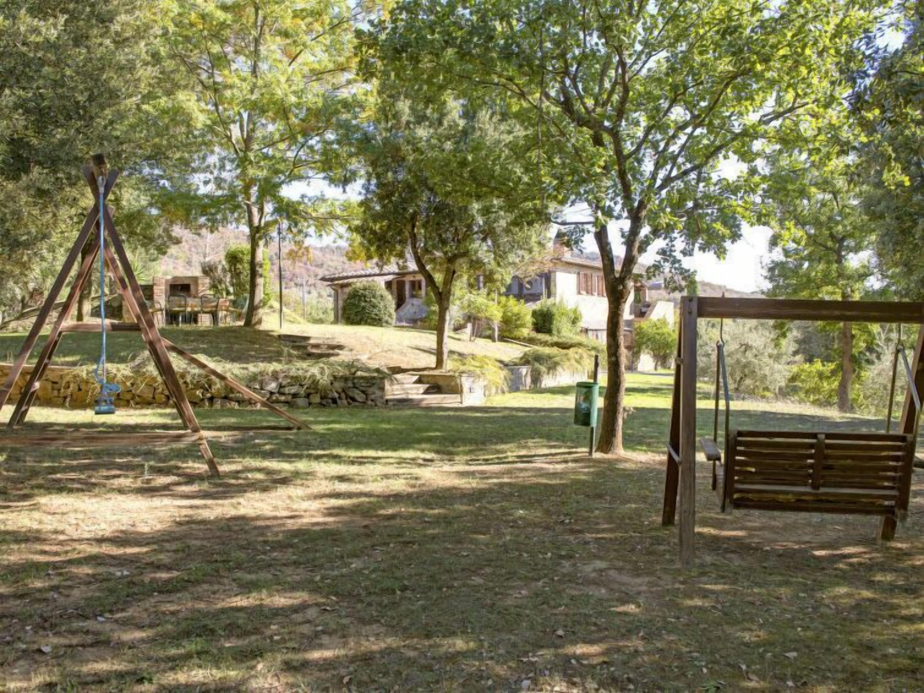 A playground with swings and a bench in a park area with trees and houses in the background.