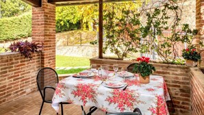 Una terrazza esterna con un muro in mattoni, un tavolo apparecchiato per mangiare e vista su un giardino.