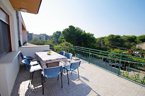 Ein Balkon mit Tisch und Stühlen, einem grünen Geländer und Blick auf Bäume und Gebäude.