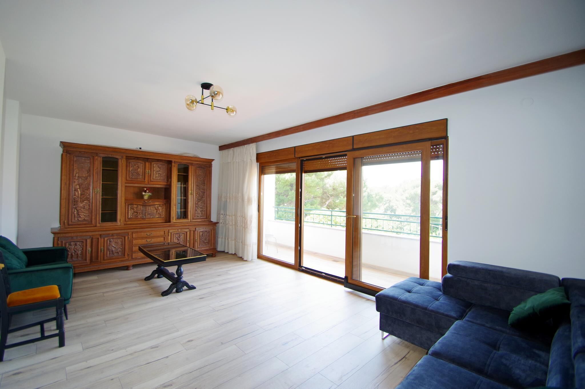 A spacious living room with a wooden cabinet, a blue sofa, and a wooden floor.