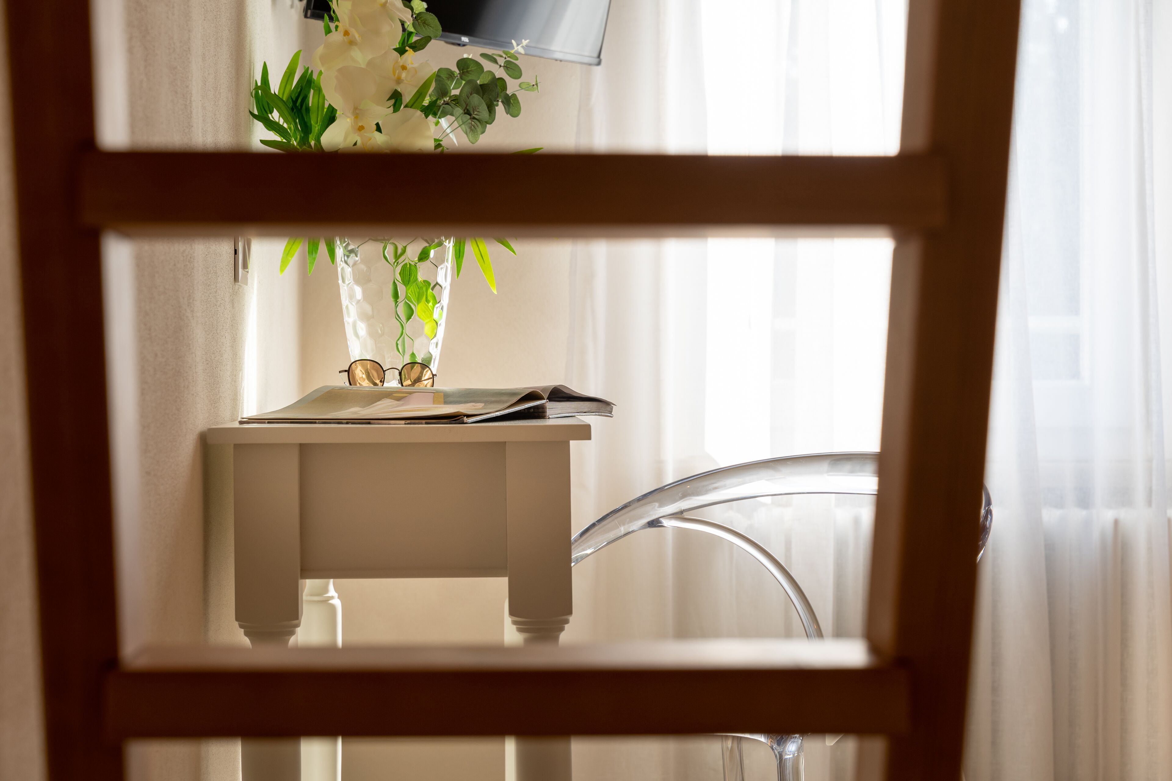 A room with a white table, a clear chair, and a window with curtains.