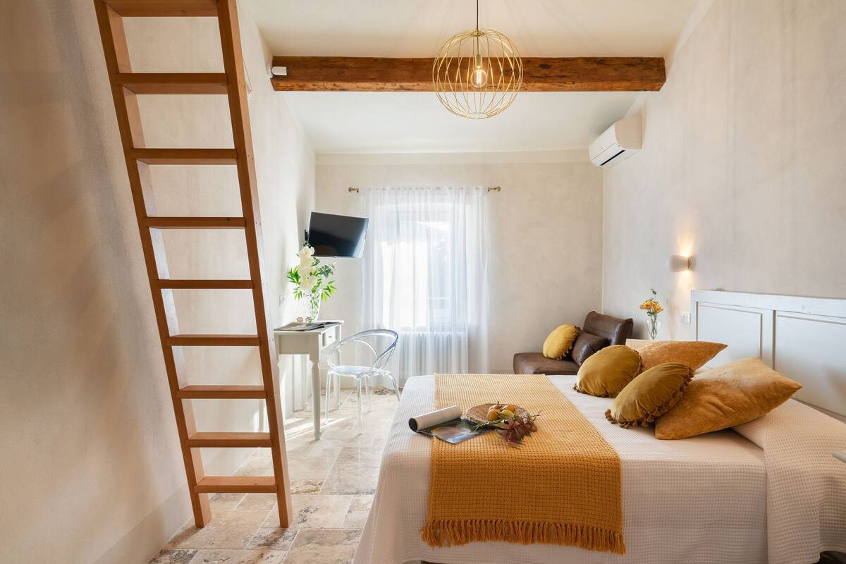 Un dormitorio con cama, escritorio, silla, televisión y una escalera.