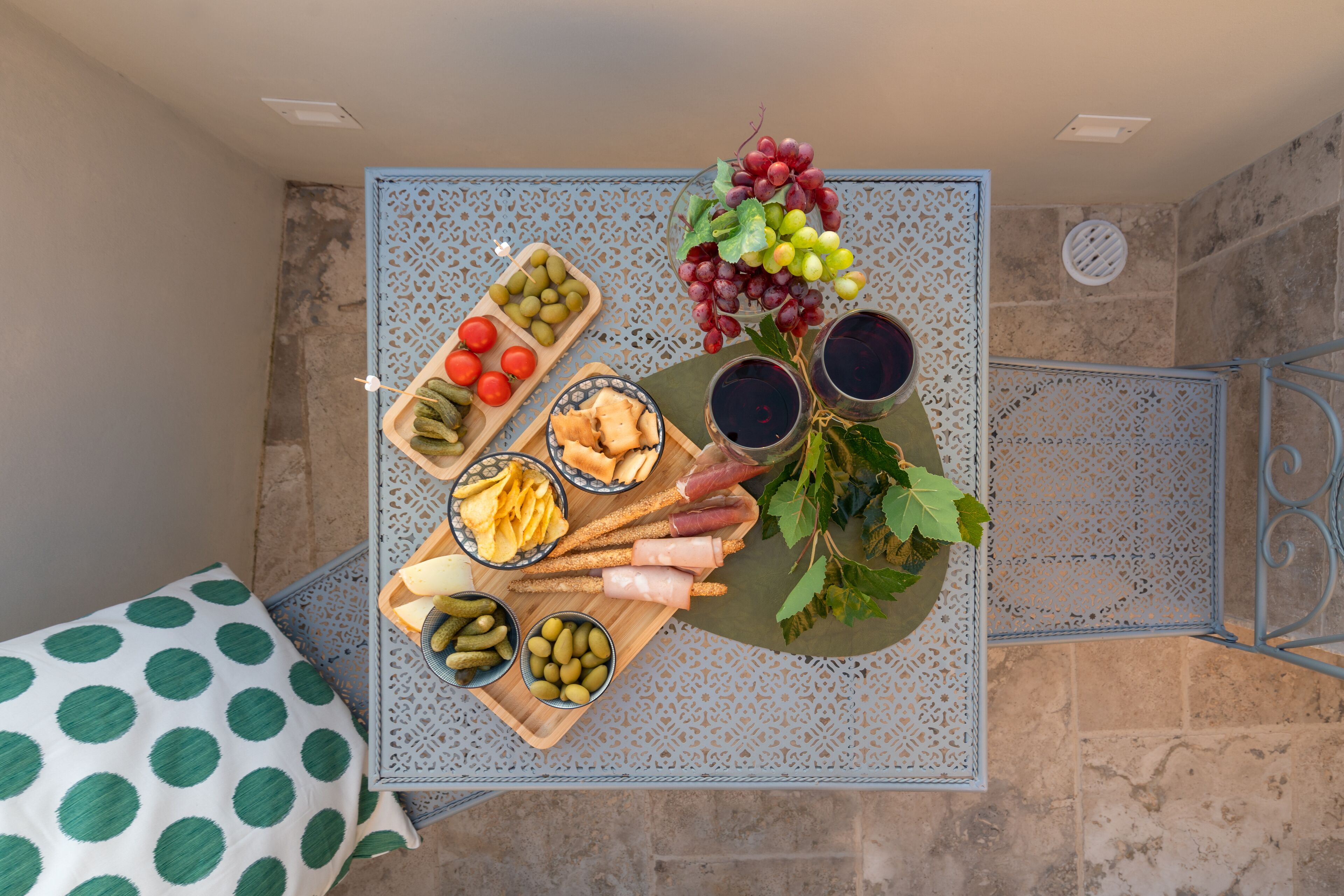 A table with a variety of food items including olives, tomatoes, grapes, breadsticks, and pickles.
