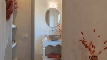 A bathroom with a round mirror, a white sink, and a vase with dried plants.