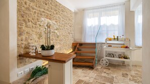 A modern kitchen with a stone wall, wooden staircase, and a breakfast bar with fruit and beverages.