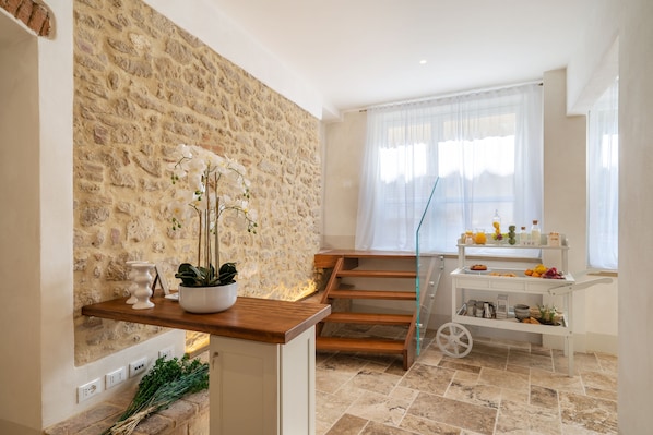 Una cucina moderna con parete in pietra, scala in legno e bancone colazione con frutta e bevande.