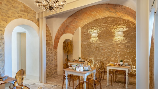 A dining area with a stone wall, wooden chairs, a table set with plates, glasses, and a fruit bowl.