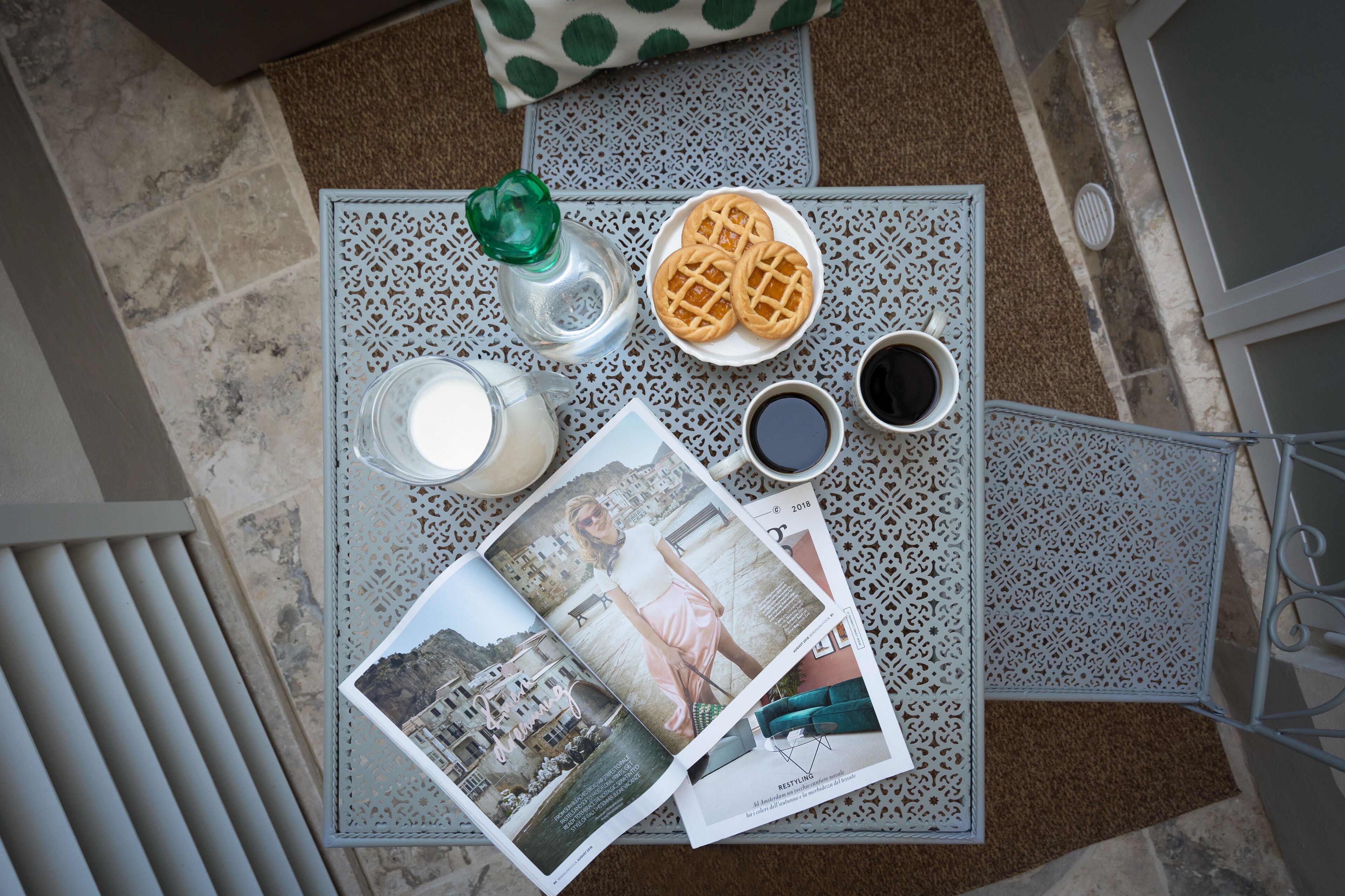 A table with a magazine, a plate of waffles, a glass of milk, a cup of coffee, and a green bottle.
