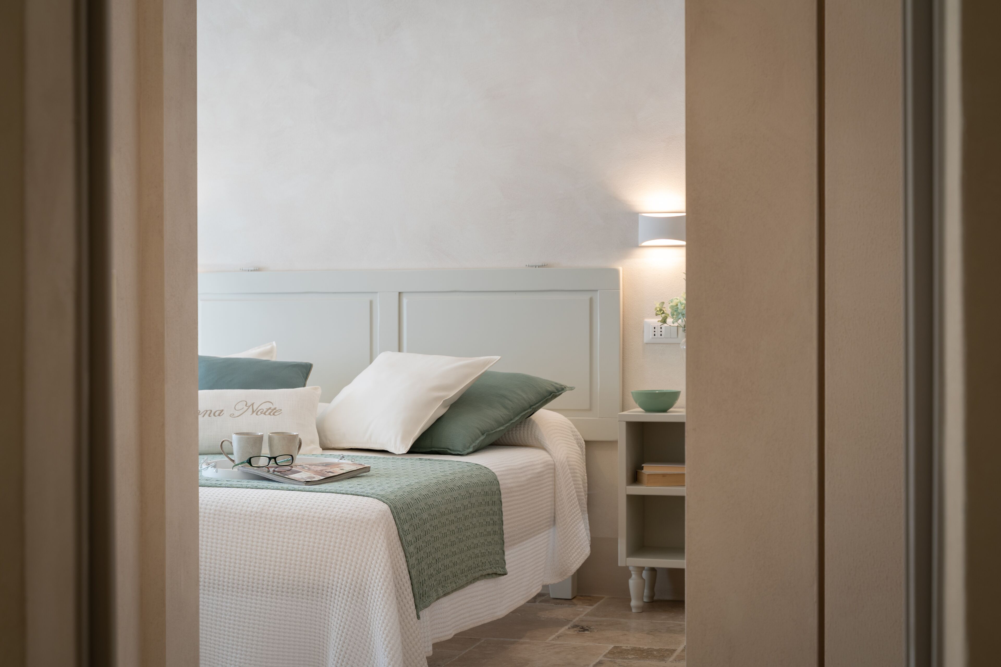 Un dormitorio con cama, almohadas, una mesita de noche y un buró.