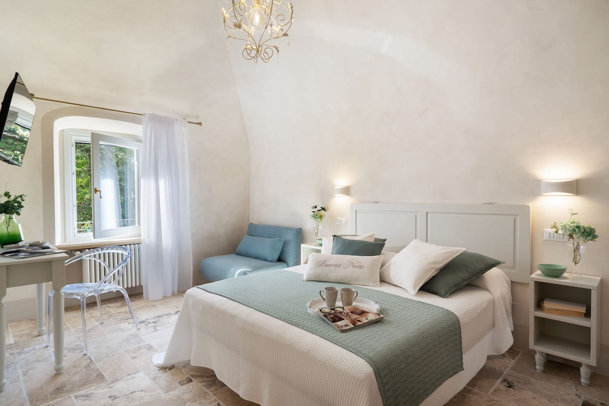 Un dormitorio con cama, mesitas de noche, escritorio, silla y ventana con cortinas.