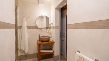 A bathroom with a wooden vanity, a round mirror, a large vessel sink, and a towel rack.