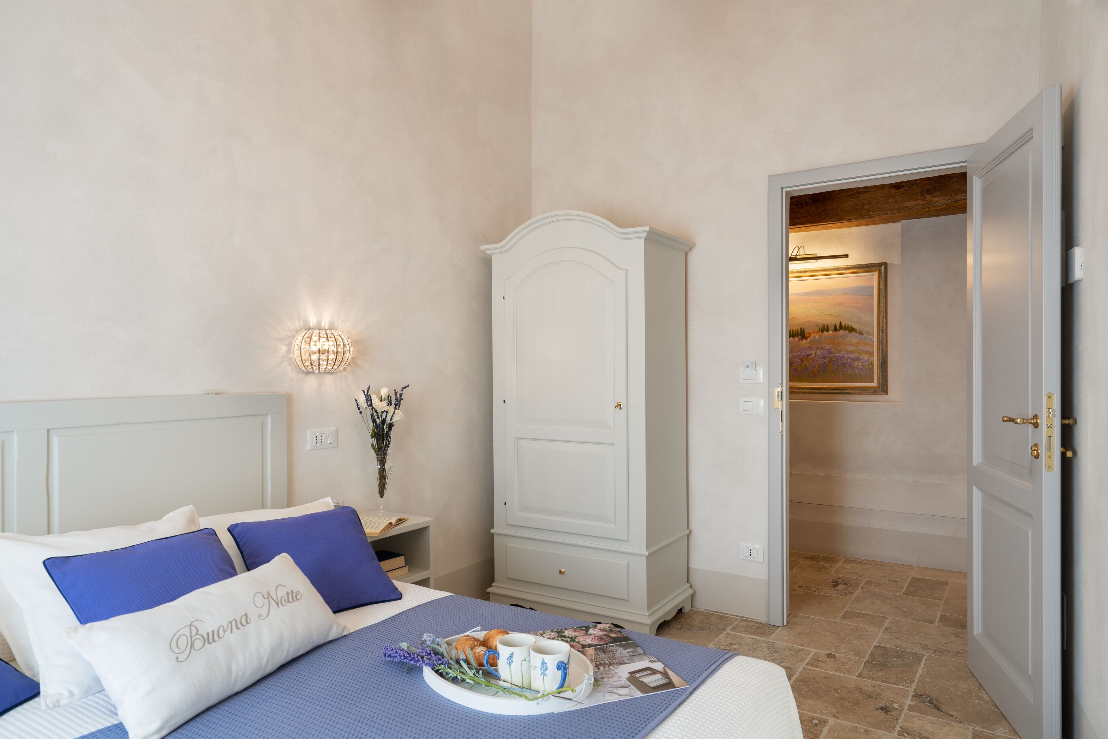 A bedroom with a bed, a nightstand, a wardrobe, and a door leading to another room.