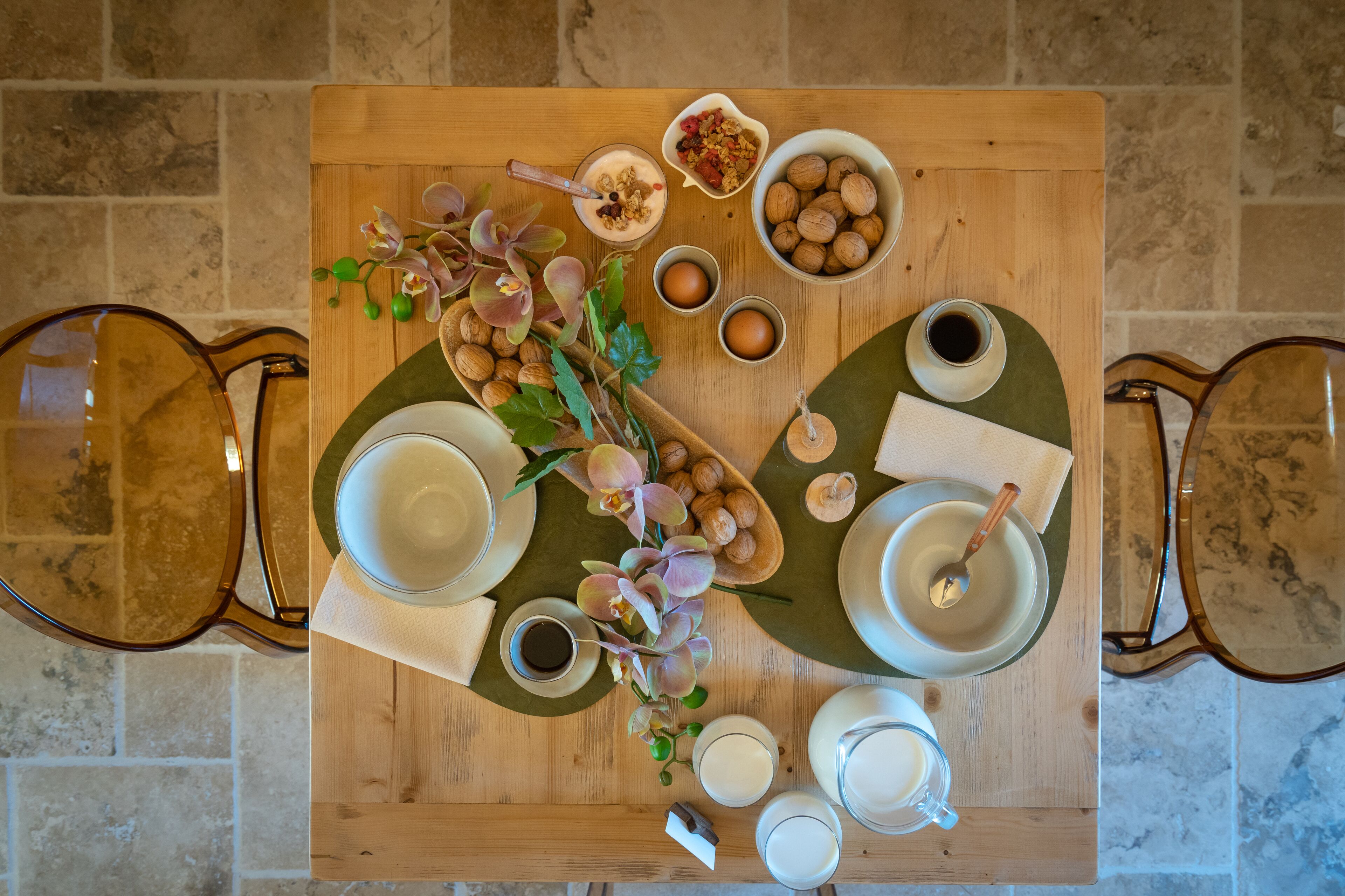 Ein Holztisch mit verschiedenen Frühstücksleckereien, darunter Eier, Nüsse und einer Blumenkomposition.