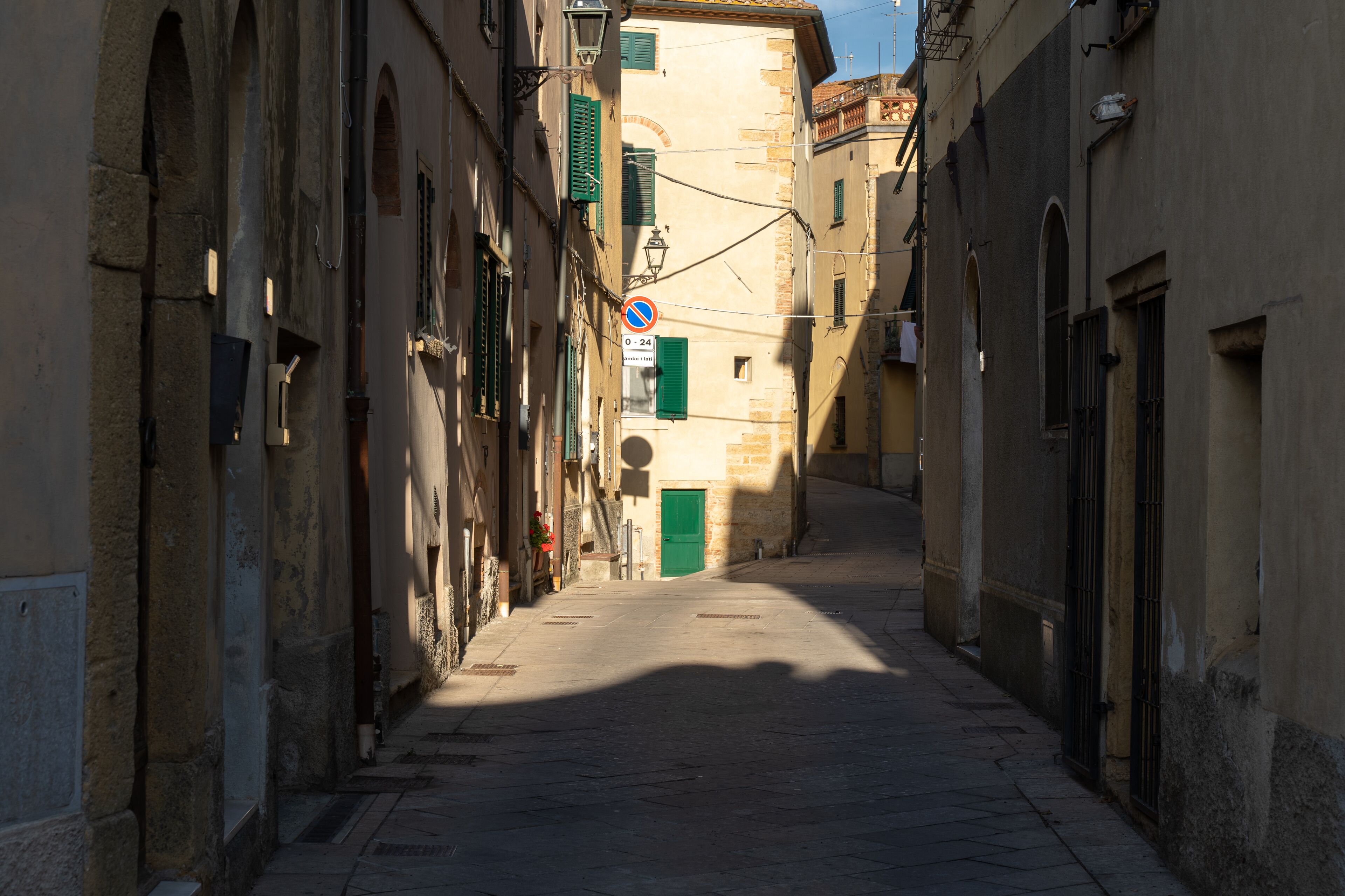 A narrow street with buildings on either side, a no parking sign, and a green door at the end.