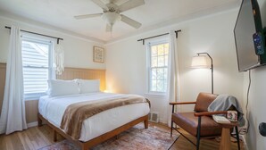 Un dormitorio con cama, una silla, ventilador de techo y televisor montado en la pared.