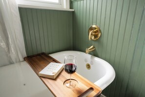 Un baño con pared verde, un lavabo blanco y una bandeja de madera con un libro y una copa de vino tinto.